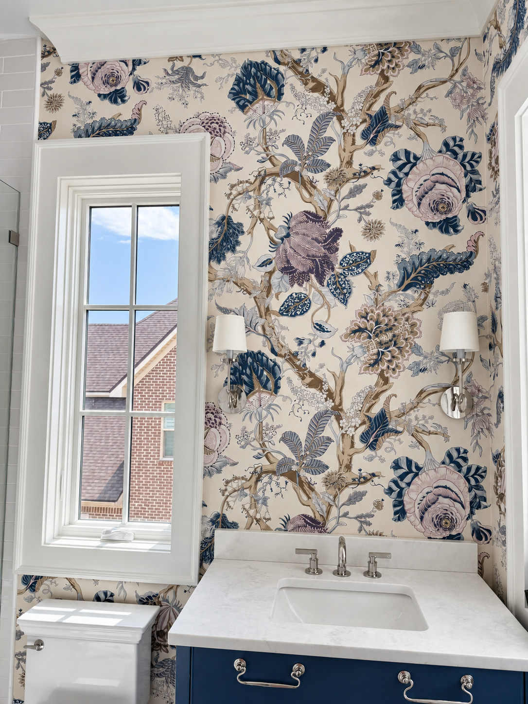 Finished powder room with large-scale blue botanical wallpaper around the window and vanity