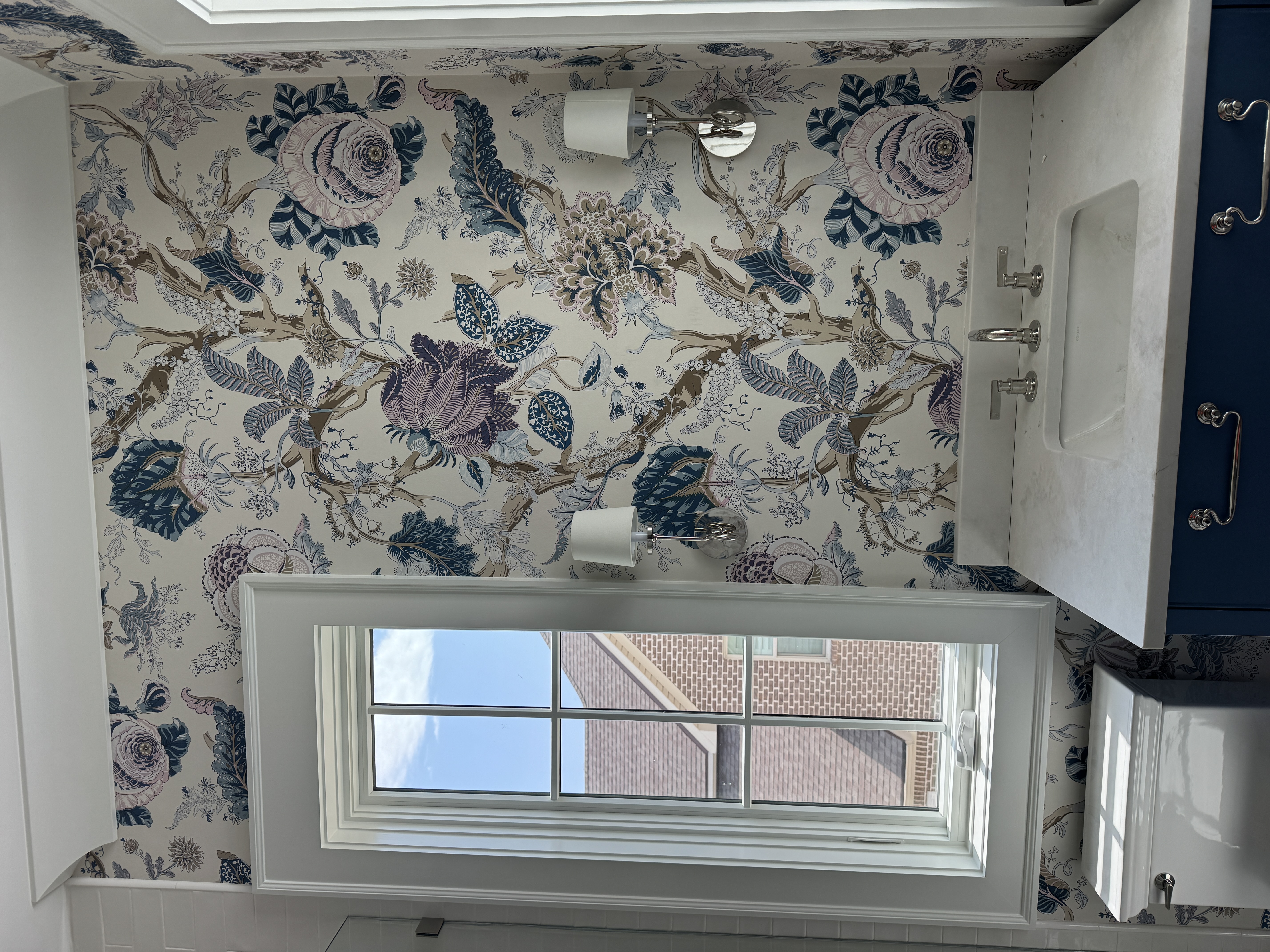 Blue and violet botanical wallpaper installed around a powder room window and vanity